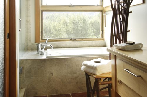 A modern bathroom featuring a soaking tub, large window, and wooden accents with neatly stacked towels.