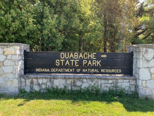 Sign for Ouabache State Park, Indiana, with stone base and greenery in the background.
