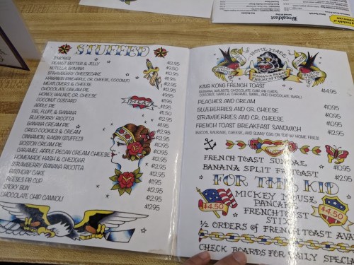 A menu page featuring various stuffed dishes, including French toast and pancakes, with colorful tattoo-style illustrations.