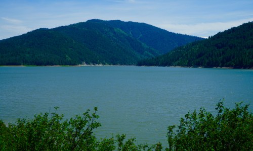 A serene lake surrounded by lush green mountains under a clear blue sky.
