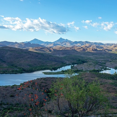 A scenic view of mountains and a lake surrounded by greenery under a partly cloudy sky.