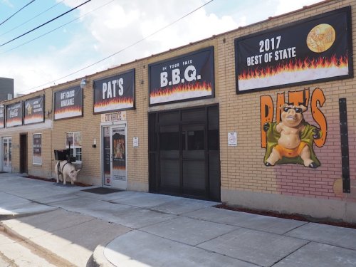 Exterior of Pat's BBQ restaurant featuring colorful signage and a cartoon pig on the wall.