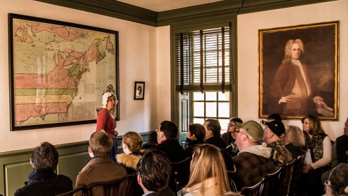 A historical presentation in a room with a large map and a portrait, featuring an audience engaged in the talk.