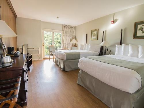 A spacious hotel room with two queen beds, a desk, and a balcony overlooking greenery.