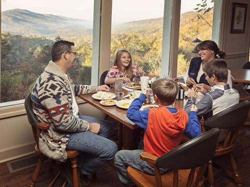 A family enjoys a meal together at a table with a scenic mountain view in the background. Laughter and joy are evident.