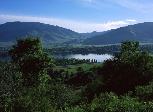 A serene landscape featuring mountains, a calm lake, and lush greenery under a clear blue sky.