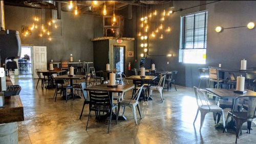 A modern dining area with wooden tables, metal chairs, and warm pendant lights hanging from the ceiling.