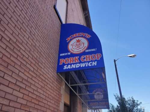 Sign for John's Pork Chop Sandwich, featuring a blue awning with the text "Home of the Pork Chop Sandwich."