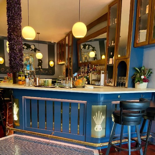 A stylish bar with a blue counter, elegant lighting, and a variety of drinks displayed on the shelves.