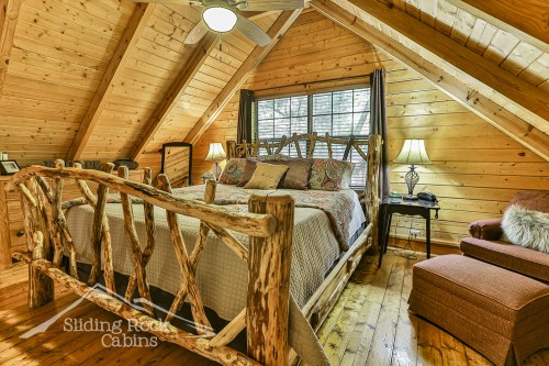 Cozy cabin bedroom with wooden walls, a log bed, and natural light from windows, featuring rustic decor and warm tones.