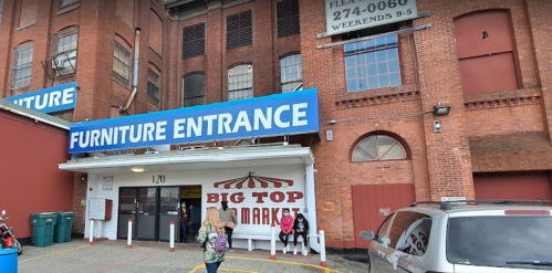 Entrance to a market with a large "Furniture Entrance" sign, featuring a red and white striped awning.