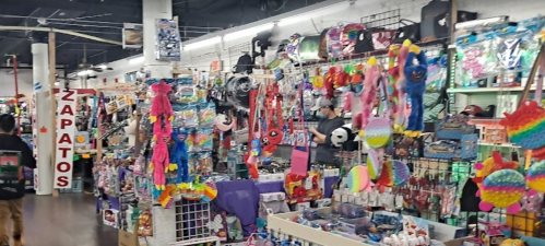 A colorful store aisle filled with various toys, accessories, and decorations, with shoppers browsing the items.