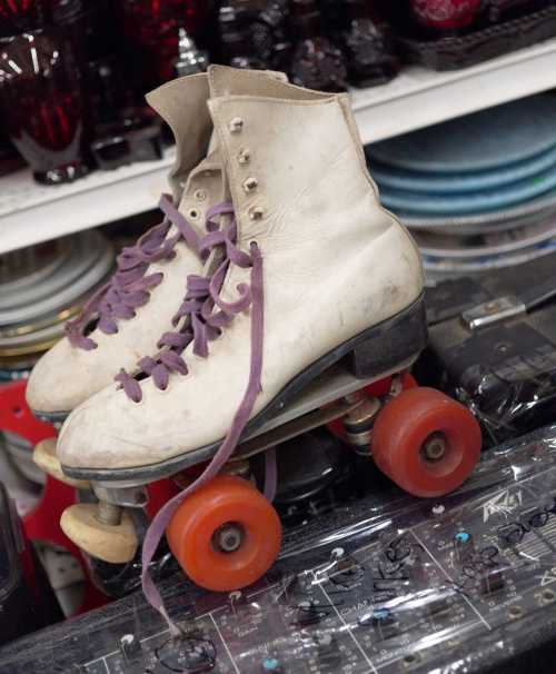 A pair of vintage white roller skates with purple laces, resting on a shelf among various collectibles.