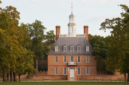 A historic brick building with a tall cupola, surrounded by trees and a grassy area.