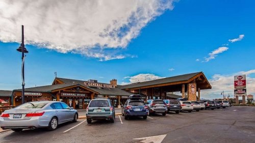 A rustic general store with a large parking lot, under a blue sky with scattered clouds.