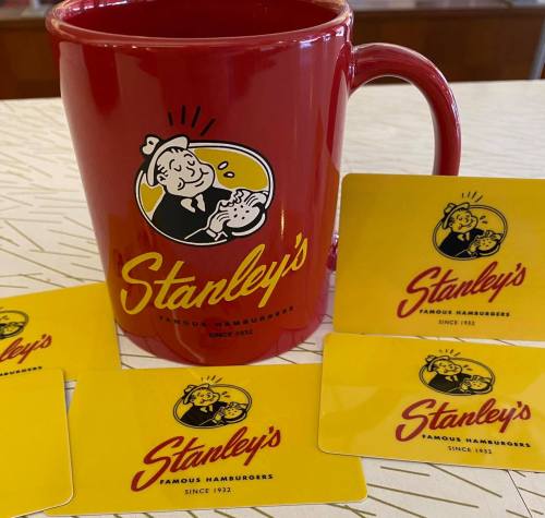 A red mug and several yellow gift cards featuring the logo of Stanley's Famous Hamburgers, established in 1932.