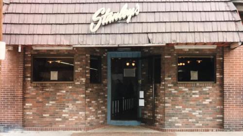Exterior of a brick building with a sloped roof, featuring a sign that reads "Stanley's" above the entrance.