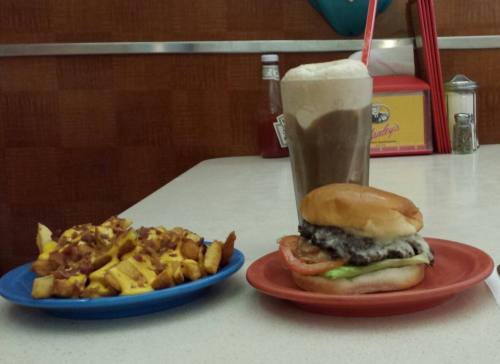 A plate with a burger topped with lettuce and tomato, alongside a plate of loaded fries and a chocolate milkshake.