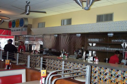 A retro diner interior featuring a colorful tiled counter, stainless steel accents, and staff behind the bar.