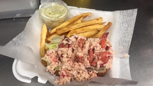 A lobster roll topped with lobster meat, served with fries and a small container of coleslaw.