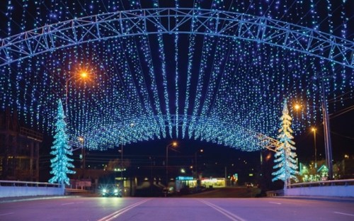 A nighttime scene featuring a street adorned with blue and white holiday lights and illuminated trees.