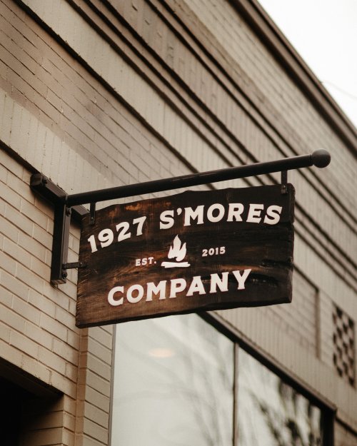 Sign for "1927 S'mores Company," established in 2015, hanging from a building.