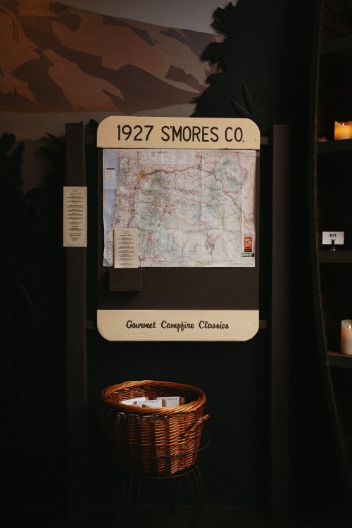 A vintage map displayed on a wall with a basket below, labeled "1927 S'mores Co. Gourmet Campfire Classics."
