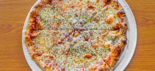 A round pizza topped with melted cheese and sprinkled with herbs, served on a silver platter against a wooden table.