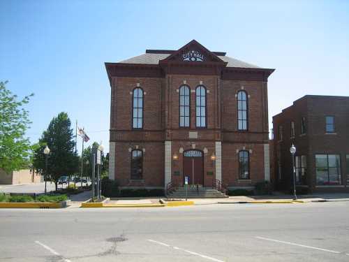 Historic brick city hall building with large windows, surrounded by trees and a clear blue sky.