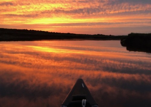 A serene sunset over a calm river, with vibrant orange and purple hues reflecting on the water's surface.