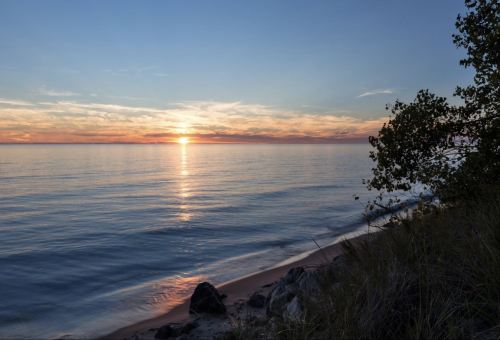 A serene sunset over calm waters, with a sandy shore and gentle waves reflecting the colorful sky.
