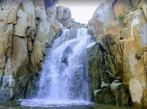 A cascading waterfall flows over rocky cliffs into a serene pool below, surrounded by natural stone formations.