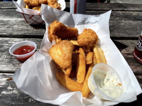 A serving of fried chicken pieces and golden fries, accompanied by dipping sauces, on a wooden table.