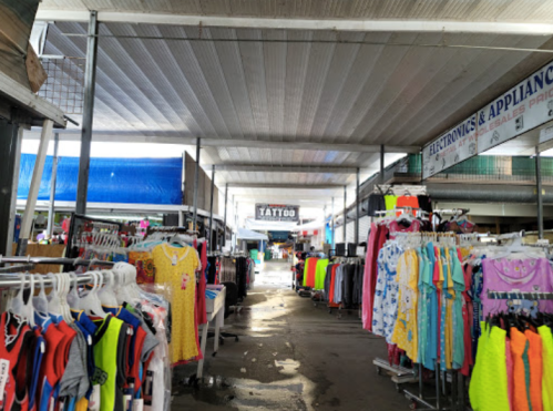 A bustling market aisle lined with colorful clothing racks under a covered structure.