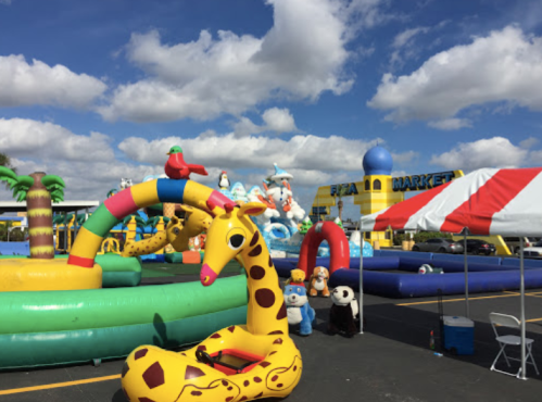 Colorful inflatable attractions, including a giraffe and various animals, under a bright blue sky with fluffy clouds.