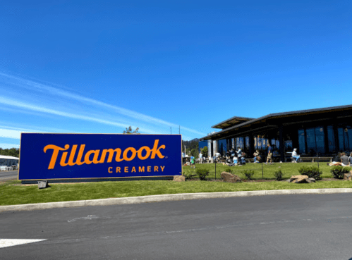 A sunny day at Tillamook Creamery, featuring a modern building and visitors enjoying the outdoor space.