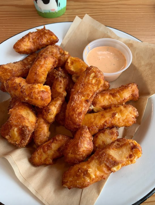 A plate of golden-brown fried snacks with a small cup of dipping sauce on a paper-lined plate.