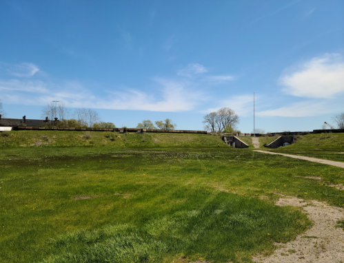 A grassy field with a clear blue sky, featuring a historic fort structure in the background.