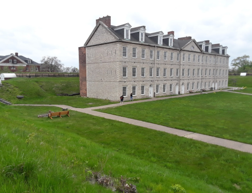 Historic stone building with multiple windows, surrounded by green grass and a pathway, under a cloudy sky.