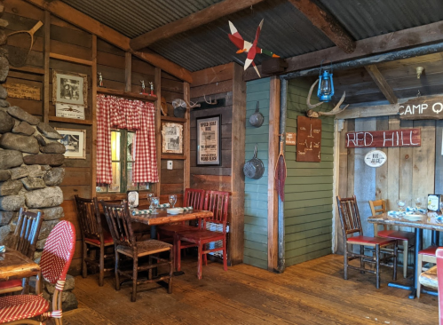 Cozy rustic restaurant interior with wooden tables, chairs, stone wall, and vintage decor. Warm, inviting atmosphere.