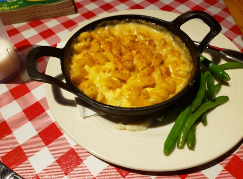 A cast iron dish of creamy macaroni and cheese, served with green beans on a checkered tablecloth.