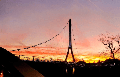 A silhouette of a cable-stayed bridge against a vibrant sunset sky with colorful clouds.