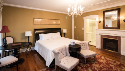 Cozy bedroom with a chandelier, a queen bed, two chairs, a small table, and an adjoining bathroom.