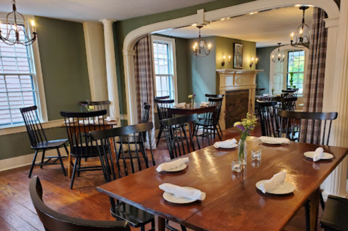 Cozy dining room with wooden tables, black chairs, and soft lighting, featuring a fireplace and floral centerpieces.