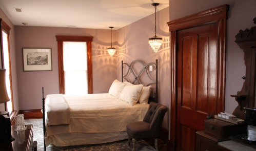 Cozy bedroom with a queen bed, elegant lighting, and vintage decor in soft purple tones.