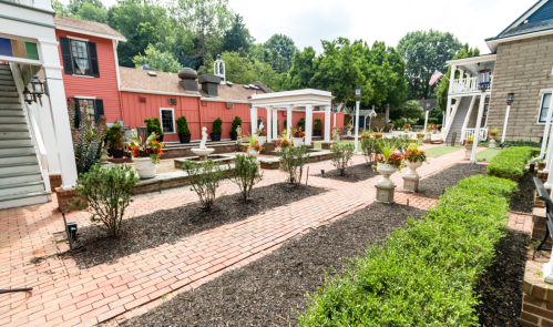 A landscaped courtyard with brick pathways, flower beds, and a fountain, surrounded by buildings and greenery.
