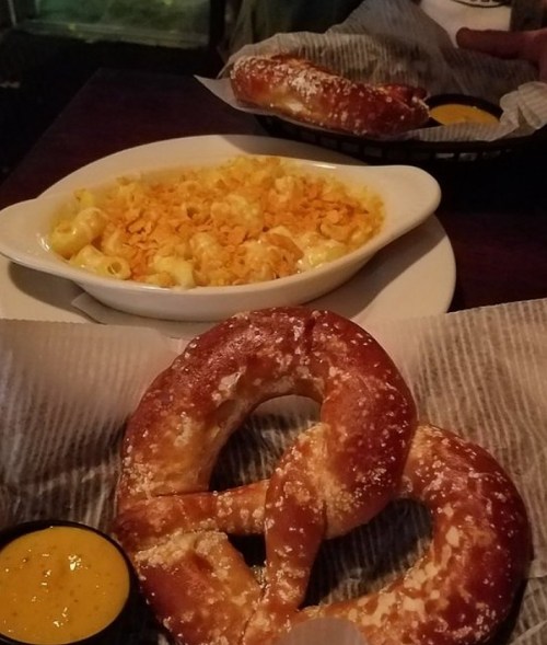 A plate with creamy macaroni and cheese and two soft pretzels served with mustard on the side.