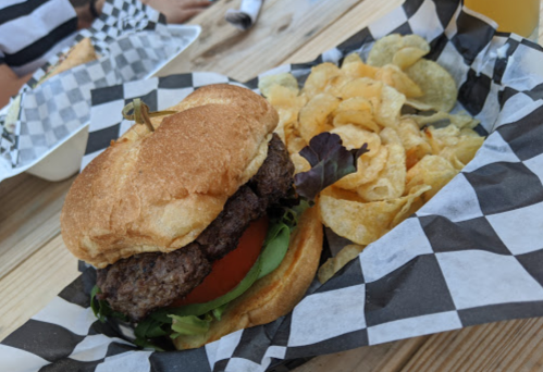 A juicy burger with lettuce and tomato, served with a side of crispy potato chips on a checkered paper.