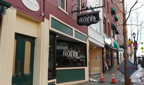A storefront with a sign reading "Nocturnem" on a city street, featuring a mix of brick and painted facades.