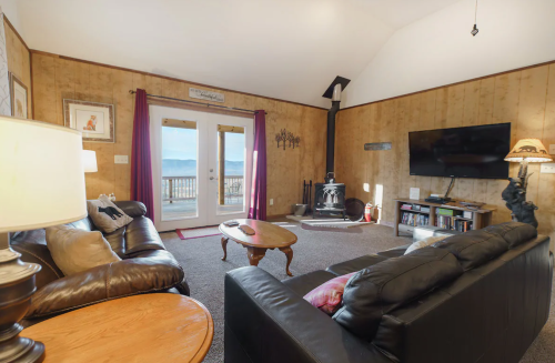 Cozy living room with wooden walls, two sofas, a TV, and a view of the outdoors through double doors.